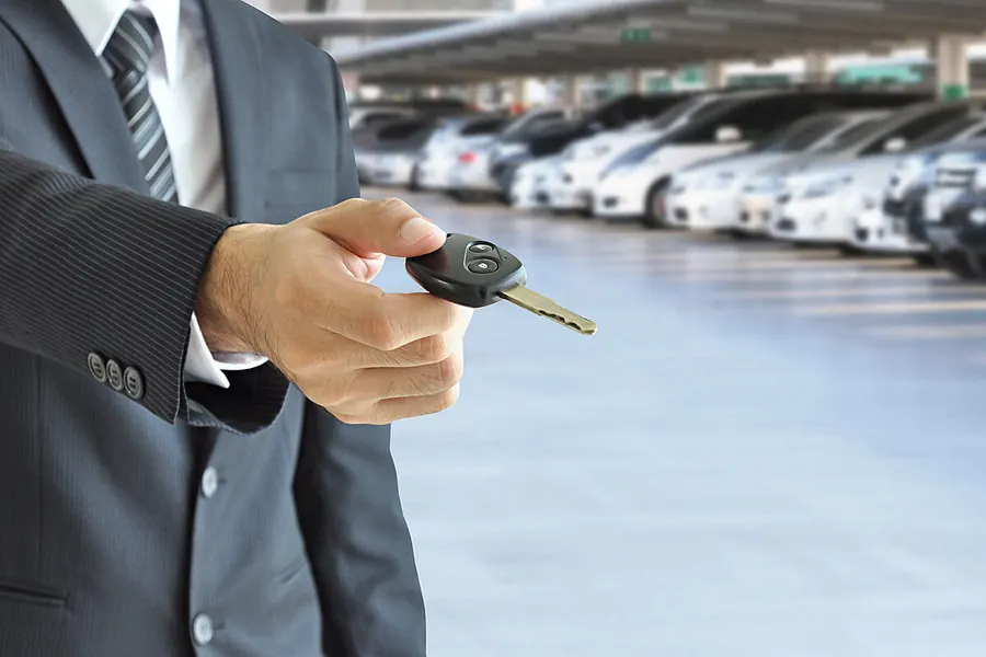 Person im Anzug reicht einen Autoschlüssel entgegen